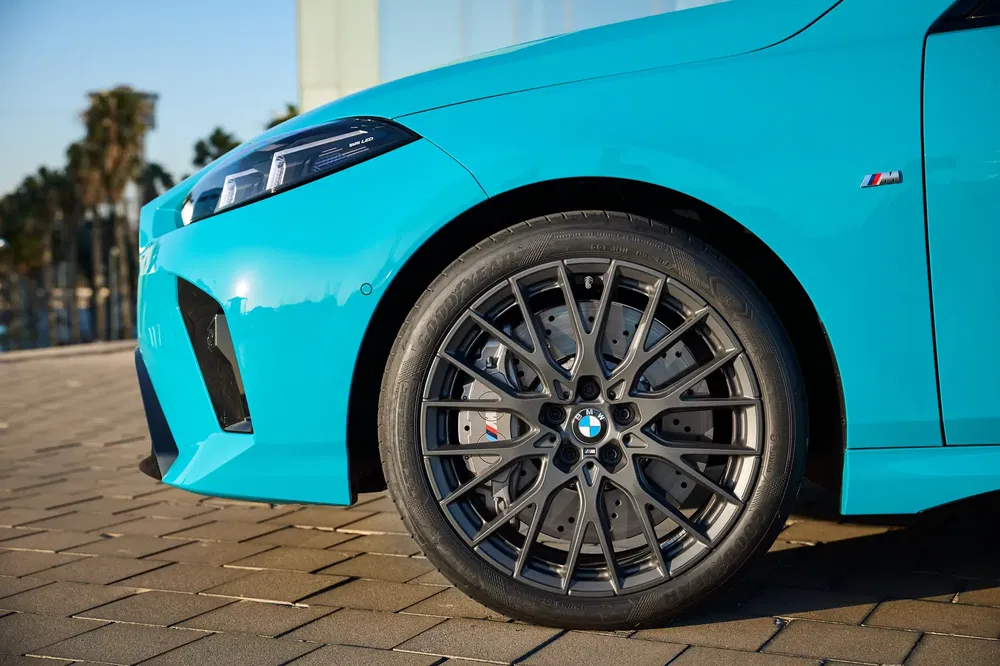Gros plan sur la roue avant d'une BMW M2 bleue en extérieur.