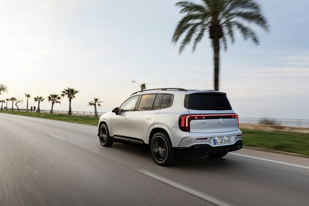 SUV Mercedes-Benz EQB électrique roulant sur une route côtière bordée de palmiers.