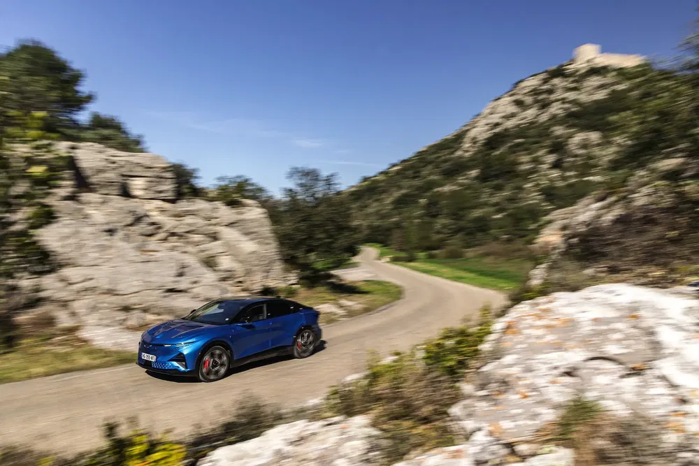 Blauwe auto rijdt op een bochtige weg omringd door rotsachtig landschap en bergen.