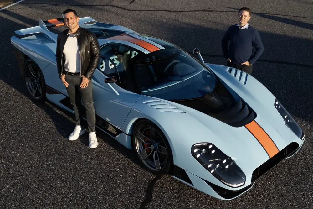 Voiture de sport Maserati MC20 bleue avec deux hommes souriants sur une piste de course.