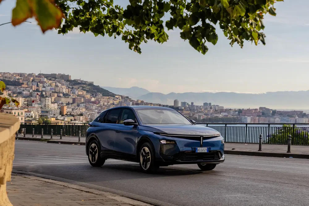 SUV Aiways U6 bleu sur route côtière avec vue sur ville en arrière-plan.