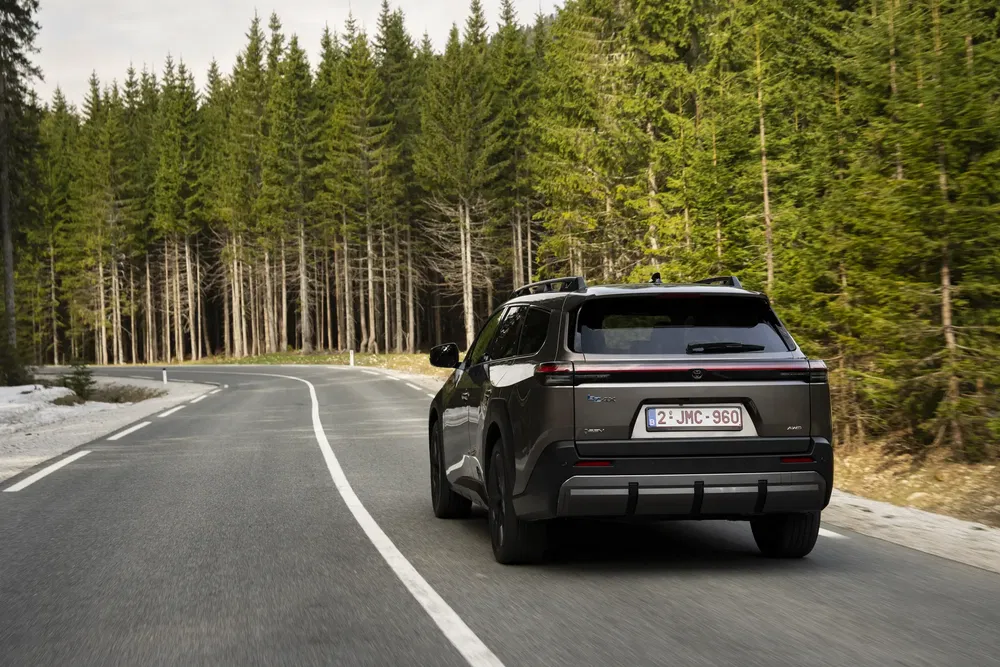SUV Toyota bZ4X sur route forestière sinueuse, arrière-plan de pins verdoyants.