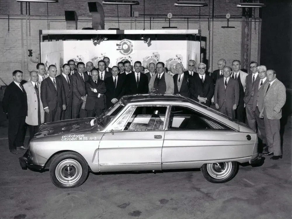 Prototype Citroën M35 entouré par un groupe de personnes posant dans un bâtiment industriel.