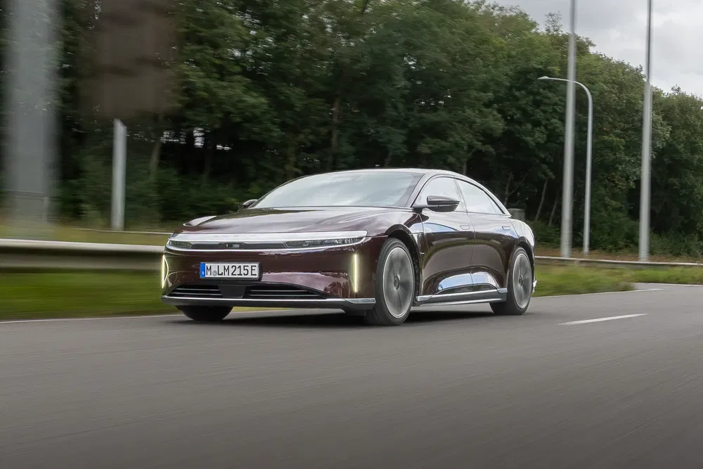 Berline électrique Lucid Air roulant sur une route bordée d'arbres.