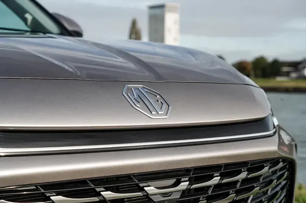 Close-up van het MG-logo op de motorkap van een stijlvolle auto, wazige achtergrond.