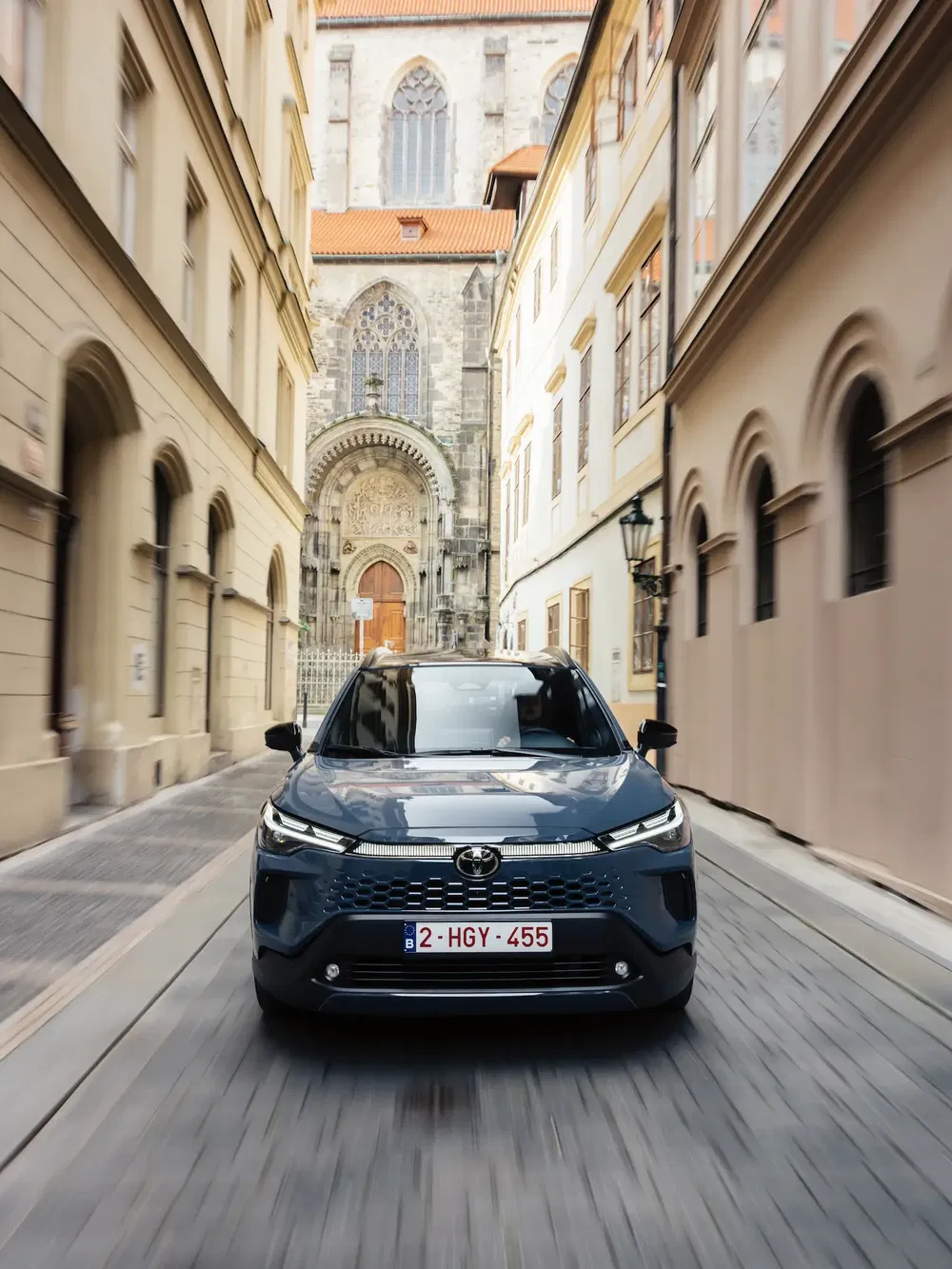 Toyota en mouvement dans une ruelle historique, architecture gothique en arrière-plan.