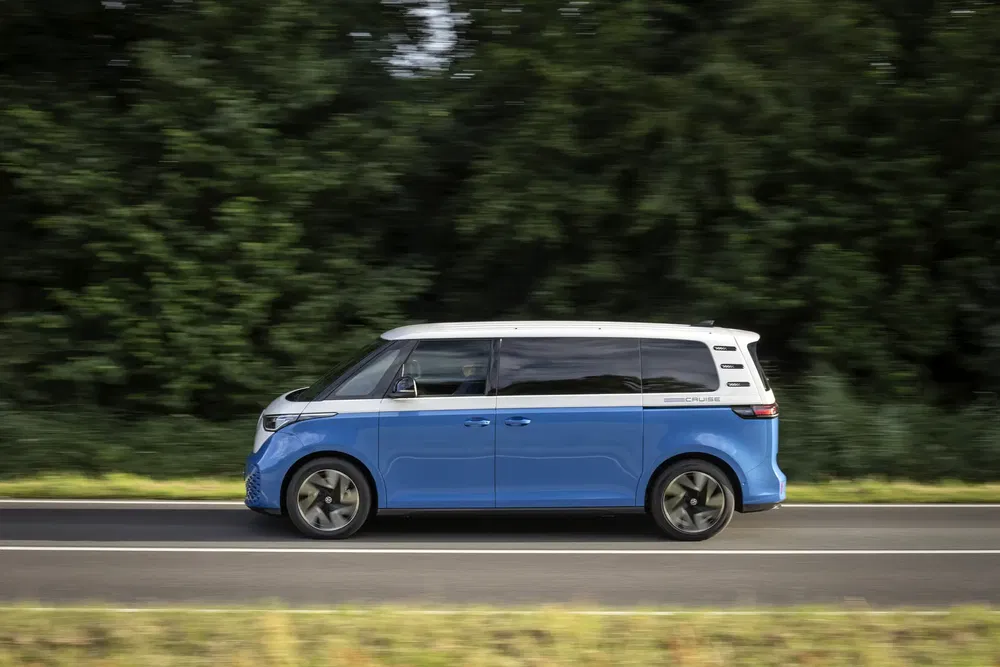 Volkswagen ID. Buzz bleu sur route, entouré de végétation luxuriante.
