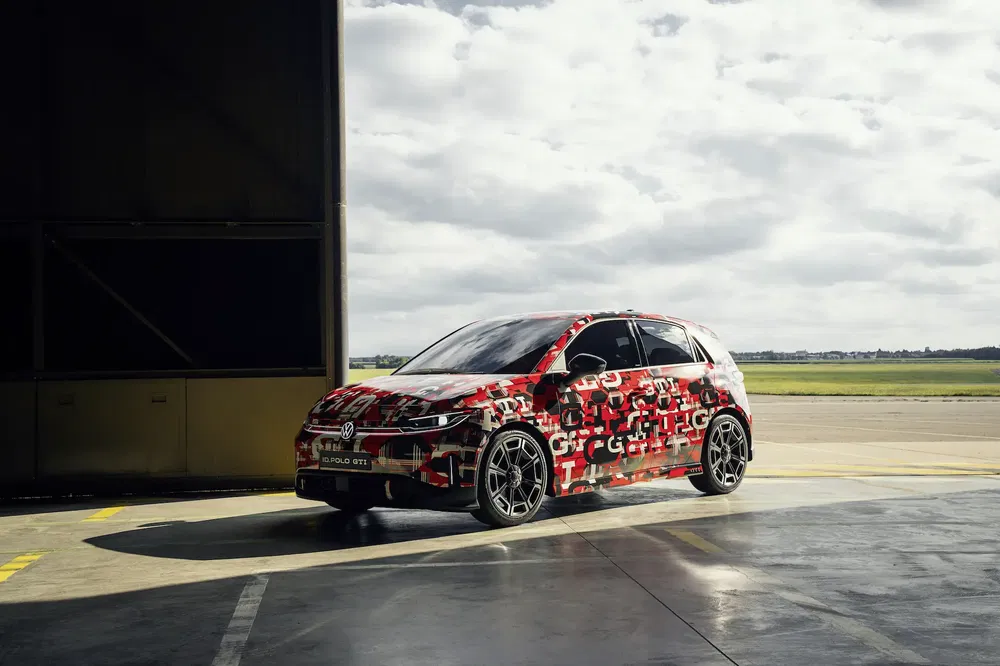 Volkswagen Golf GTI camouflée garée dans un hangar, ciel nuageux en arrière-plan.