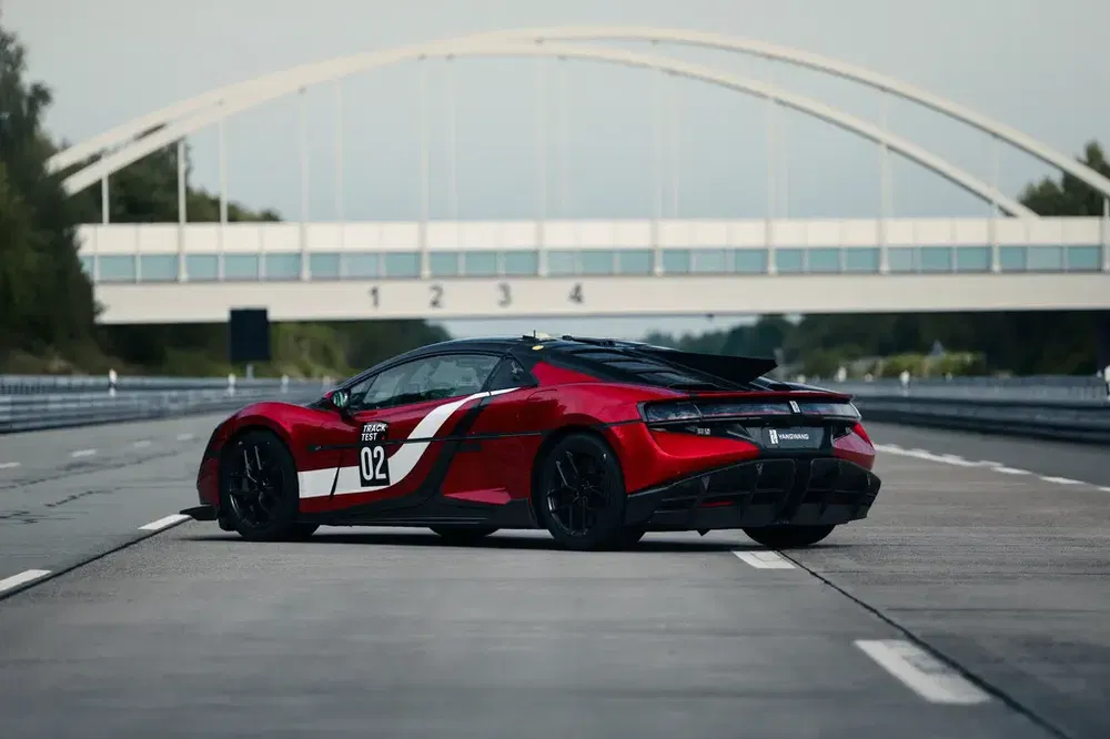 Rode McLaren sportwagen op circuit met brug op de achtergrond.