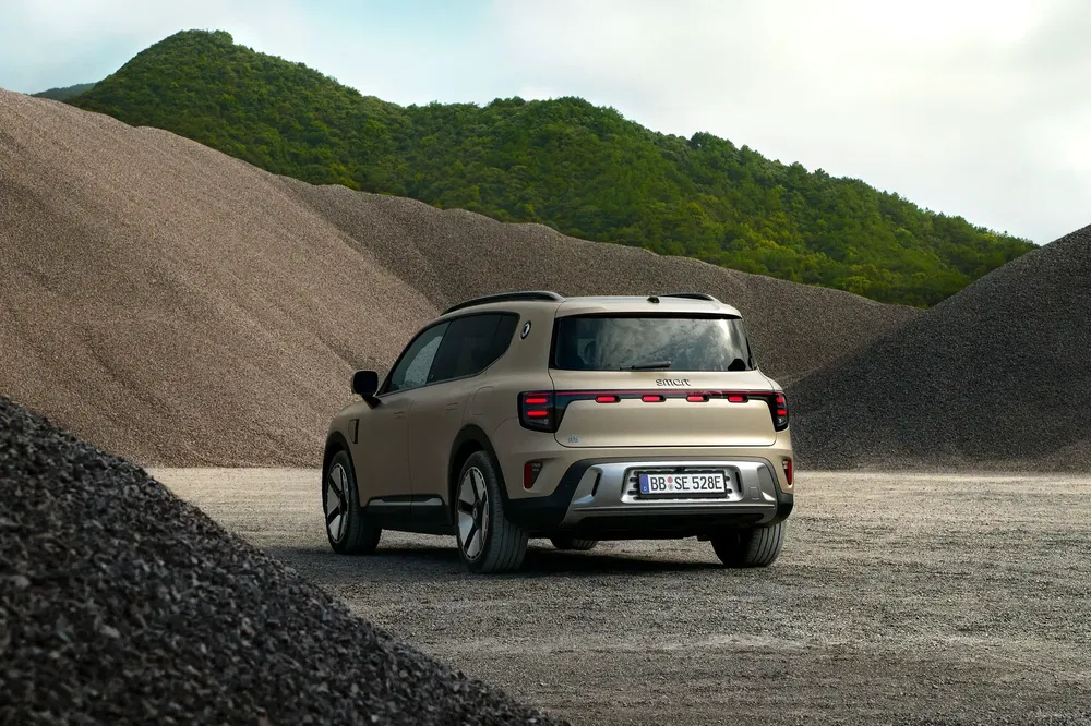Beige elektrische SUV Scout geparkeerd op een grindterrein met groene heuvels op de achtergrond.