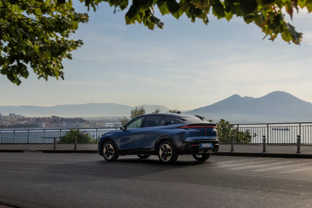 SUV bleu Lancia Pu+Ra HPE devant paysage côtier et montagnes en arrière-plan.