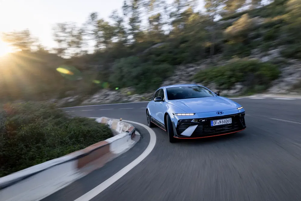 Hyundai Ioniq 6 bleu sur route sinueuse au coucher du soleil, arbres en arrière-plan.