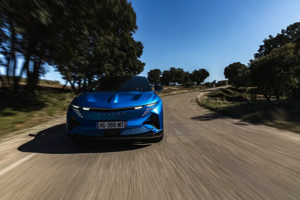 Blauwe Alpine auto rijdt op landelijke weg onder heldere hemel.