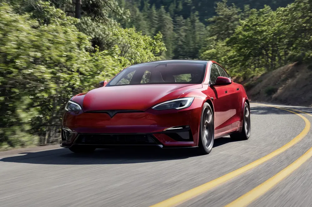Rode Tesla Model S op een schilderachtige weg omgeven door weelderige bomen.