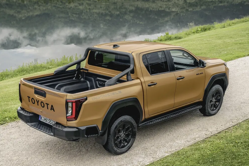 Toyota Hilux doré, pick-up robuste au bord d'un lac, arrière et latéral visibles.