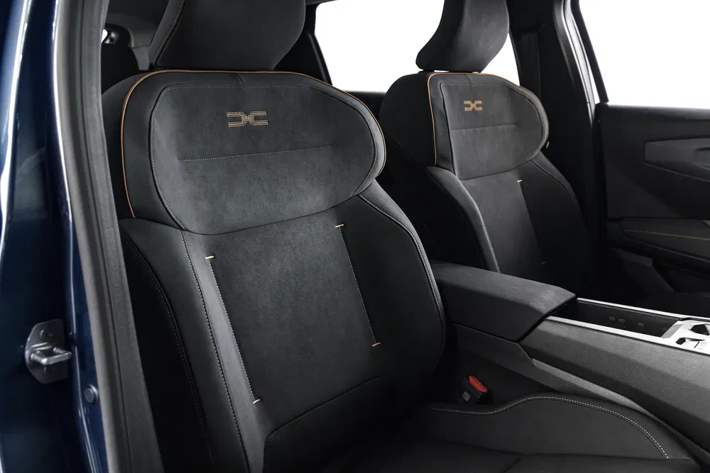 Moderne auto-interieur met zwarte stoelen en oranje stiksels, DXE-logo op hoofdsteun.