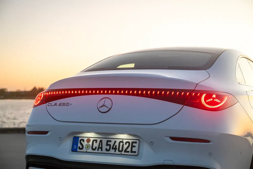Achteraanzicht van een Mercedes-Benz CLA 250e plug-in hybride bij zonsondergang.