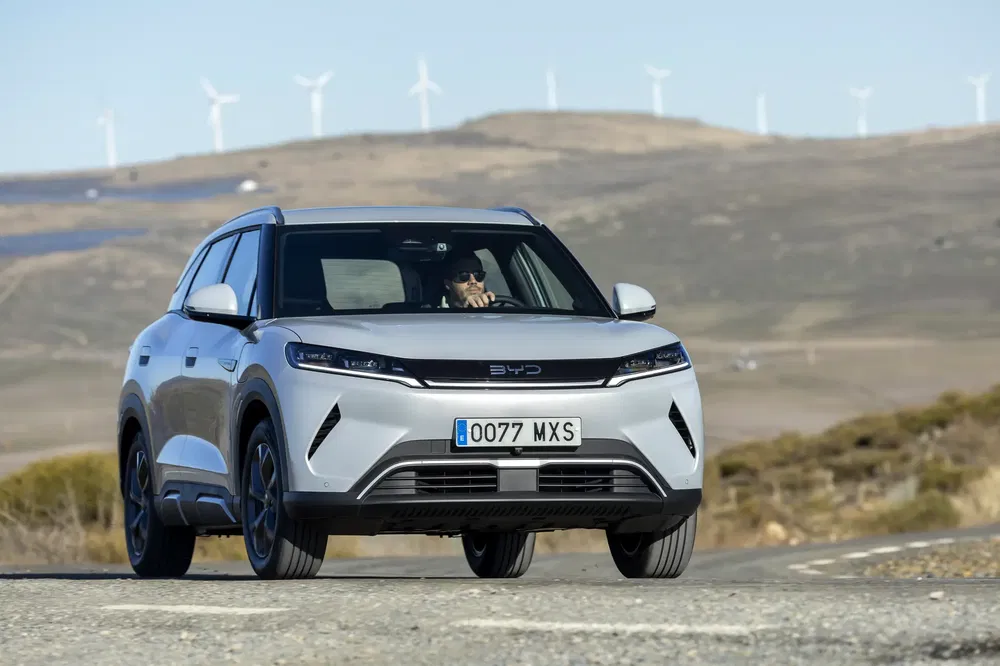SUV BYD blanc sur route de campagne avec éoliennes en arrière-plan.