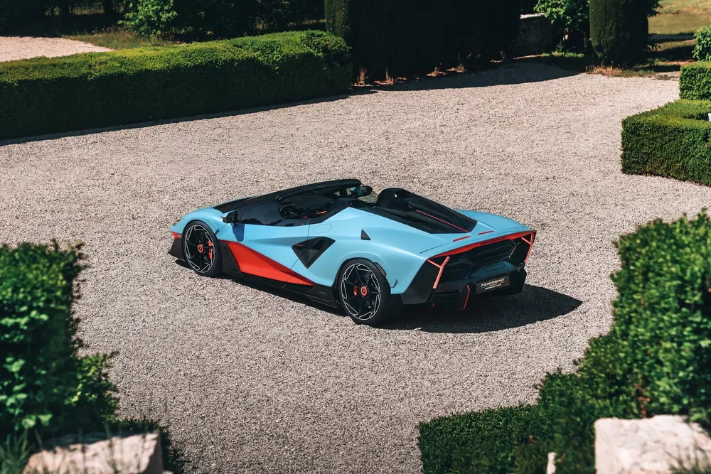 Achteraanzicht van een blauwe en rode Lamborghini SC20 geparkeerd op grind.