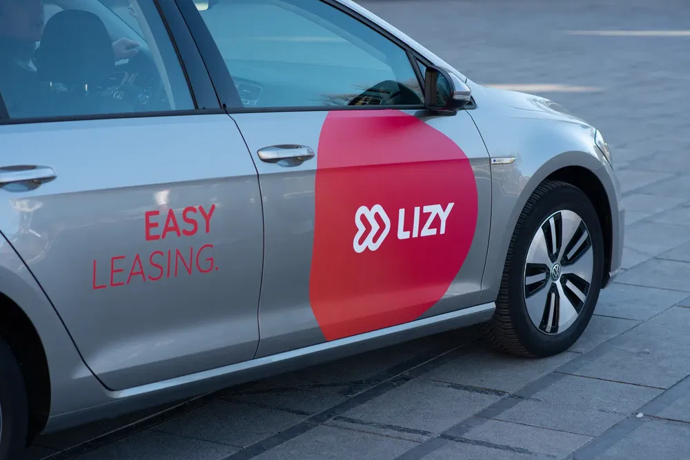 Volkswagen-auto met Lizy-logo, gericht op eenvoudig leasen, geparkeerd op stedelijke bestrating.