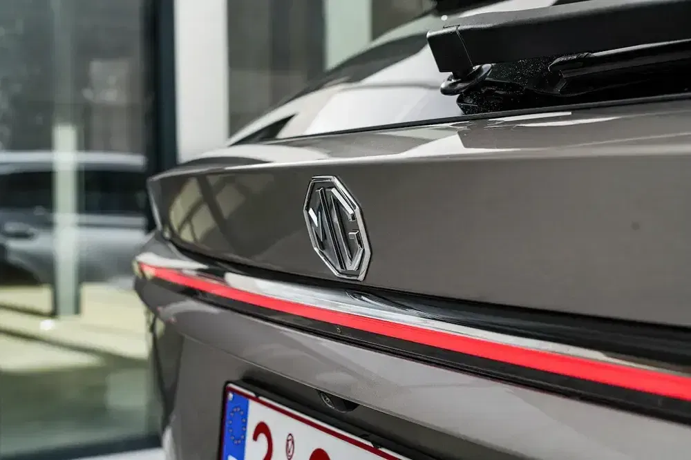 MG-logo op de achterkant van een grijze, moderne auto in een showroom.