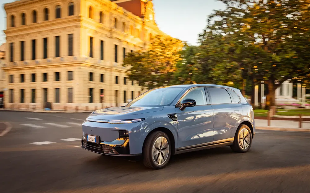 SUV électrique moderne traversant un carrefour urbain ensoleillé, architecture européenne en arrière-plan.