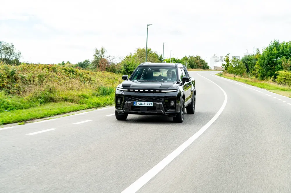 Zwarte SUV rijdend op een landelijke weg, met een groen landschap op de achtergrond.
