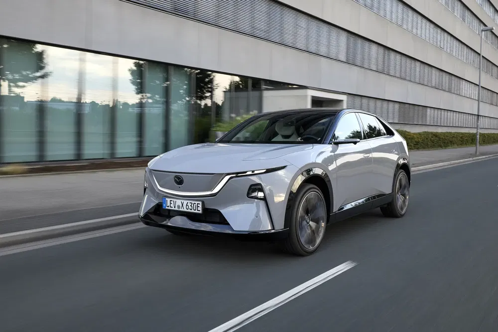 Voiture électrique de luxe argentée roulant devant un bâtiment moderne.