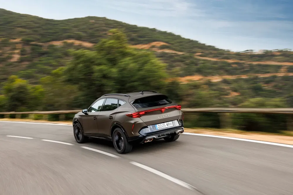 Cupra Formentor marron roulant sur route montagneuse sinueuse, vue arrière dynamique.