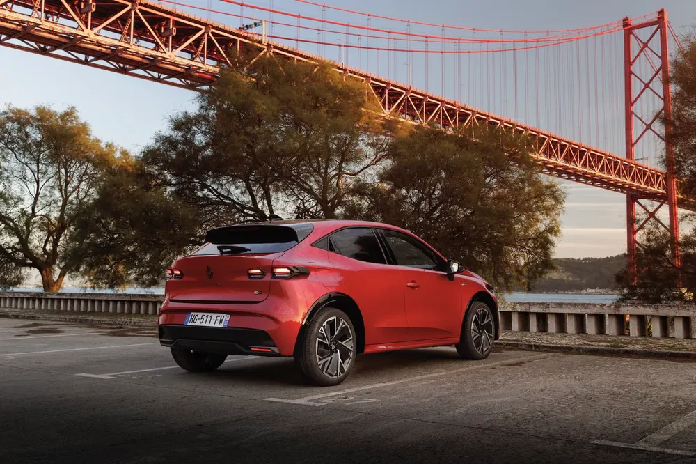 Renault Mégane électrique rouge sous un pont suspendu, arrière-plan naturel.
