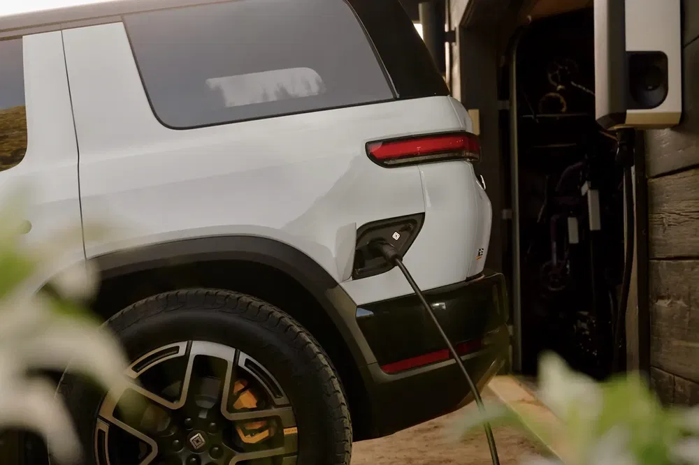 Voiture électrique Rivian chargée dans un garage moderne, câble connecté à la prise arrière.