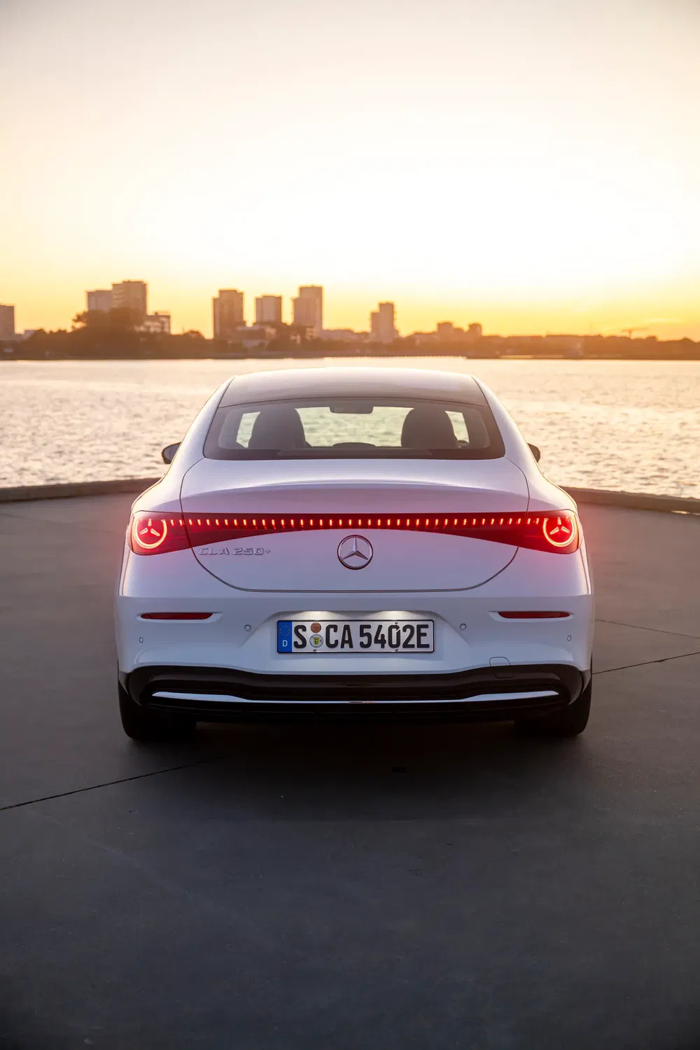 Achteraanzicht van een Mercedes CLA 250 e bij zonsondergang aan het water.