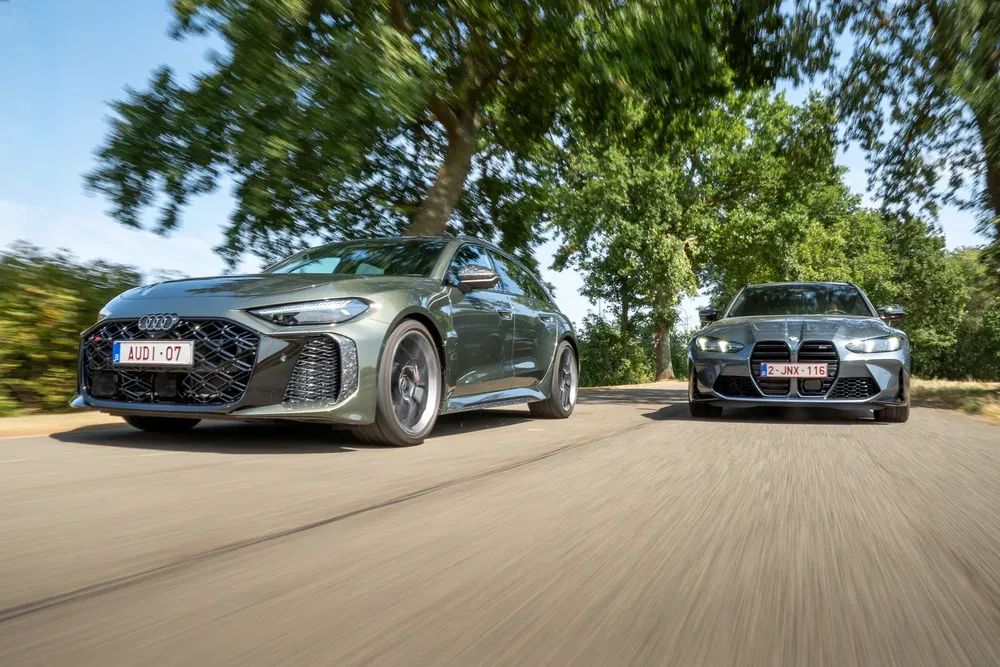 Twee sportwagens, Audi en BMW, rijden samen op een met bomen omzoomde weg.