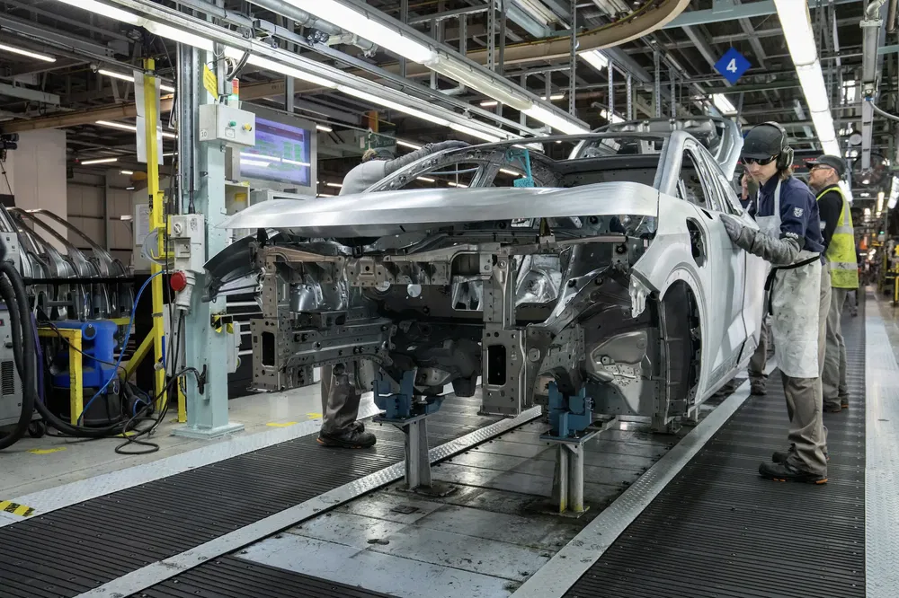Chaîne de montage automobile avec employés assemblant un châssis de voiture dans une usine moderne.