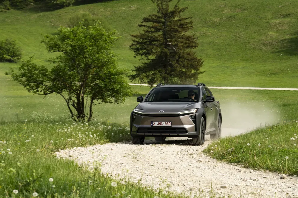 Toyota bZ4X électrique sur chemin de gravier, paysage verdoyant en arrière-plan.