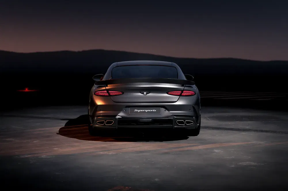 Bentley Supersports grise sur route, silhouettée par un ciel nocturne.