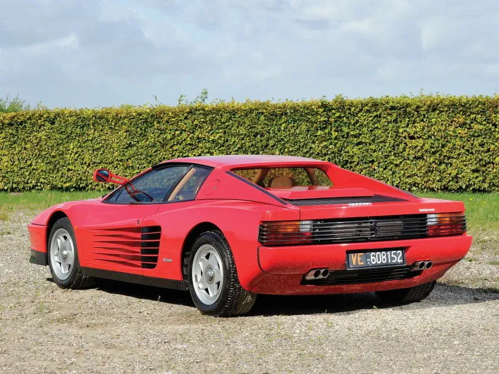 Rode Ferrari Testarossa geparkeerd voor groene haag, duidelijk zicht op achterkant.