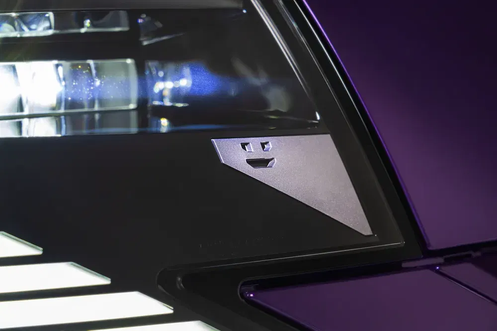 Gros plan sur le phare d'une voiture avec un logo en relief, fond sombre.