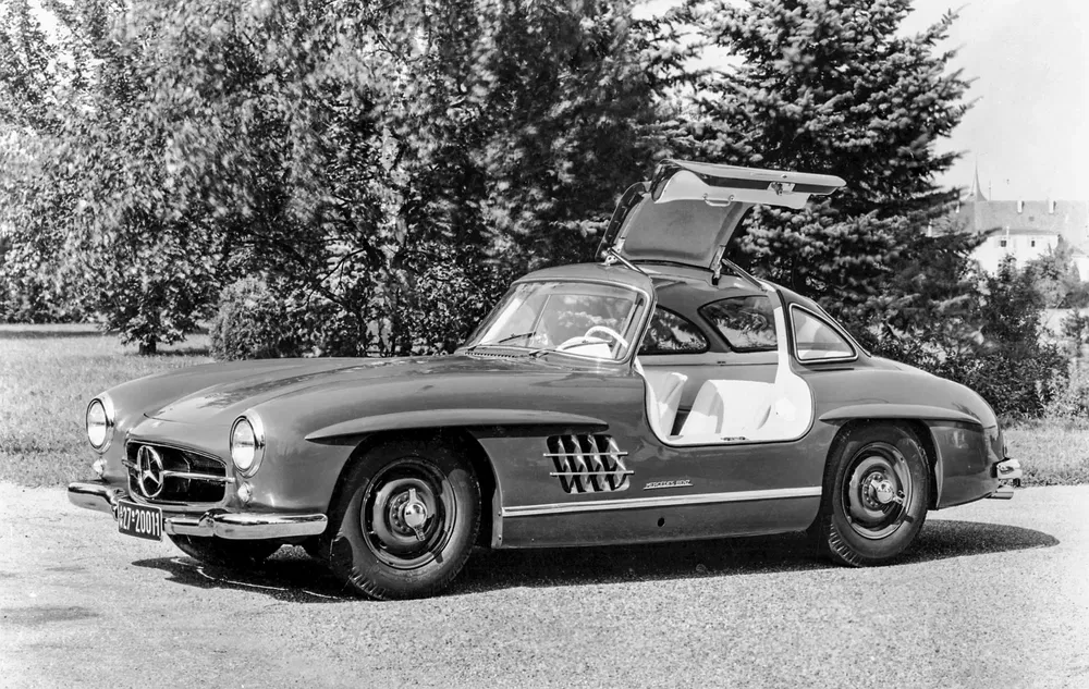 Mercedes-Benz 300SL classique avec portes papillon ouvertes, stationné près d'arbres.