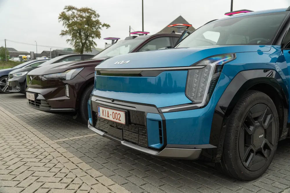 Alignement de voitures, en avant une Kia EV9 bleue sur une aire de stationnement.