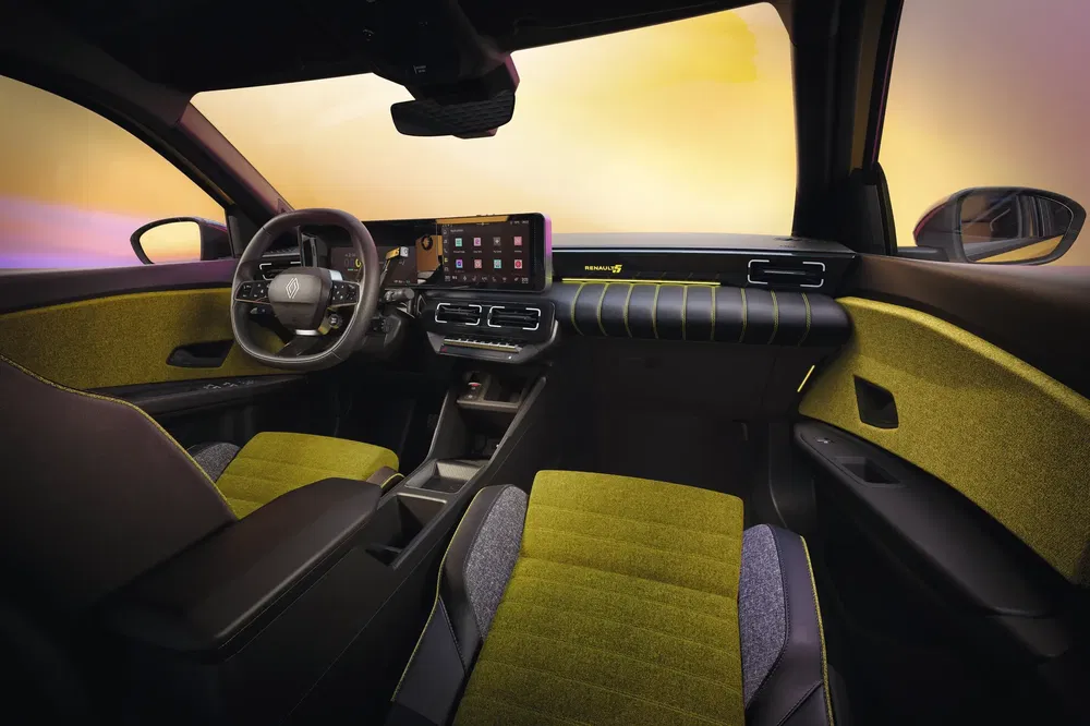 Moderne interieur van de Renault 5 met digitaal dashboard en groene stoffen stoelen.