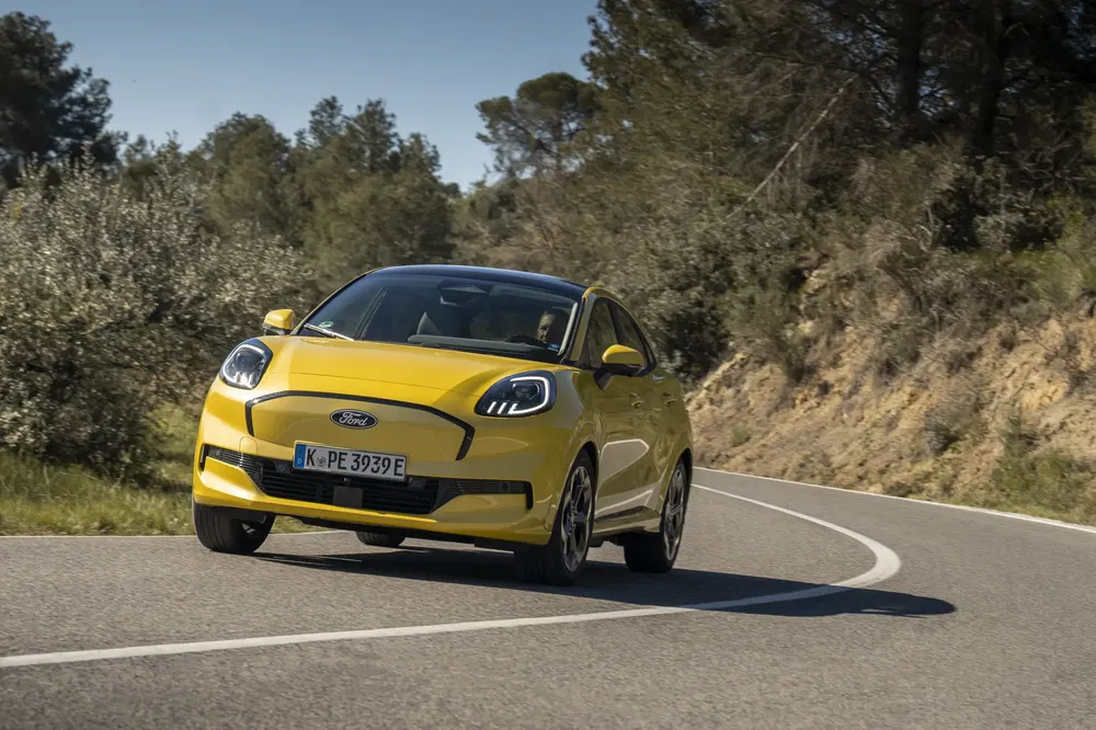 Ford Puma électrique jaune sur route sinueuse entourée de végétation et arbres.