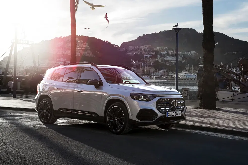 Mercedes-Benz GLB blanc garé près du port avec arrière-plan montagneux et coucher de soleil.