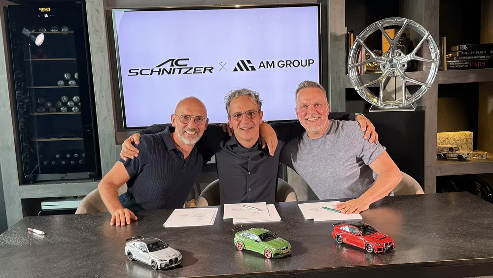 Trois hommes signent un contrat, maquettes de voitures AC Schnitzer sur la table.