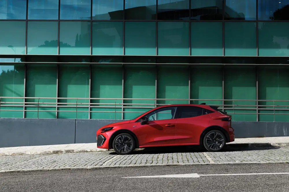 Voiture électrique rouge garée devant un immeuble moderne aux vitres réfléchissantes.
