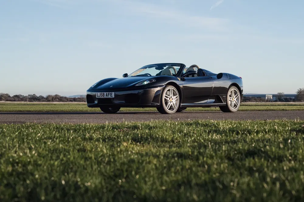 Ferrari F430 Spider noire garée sur piste d'aviation sous un ciel dégagé.