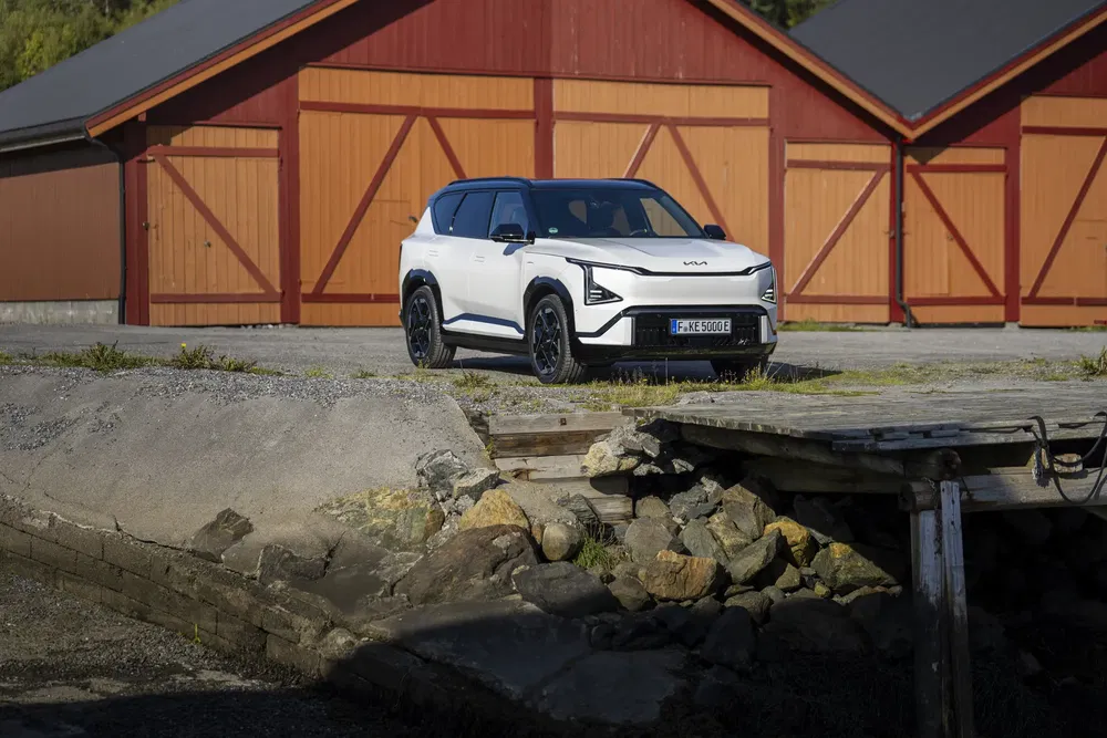 SUV Kia moderne stationné devant des garages en bois rouge, design avant angulaire distinctif.