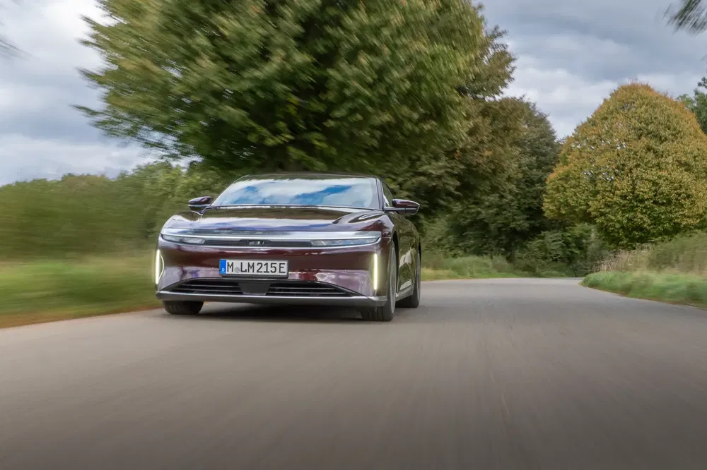La Lucid Air électrique en mouvement sur une route bordée d'arbres verdoyants.