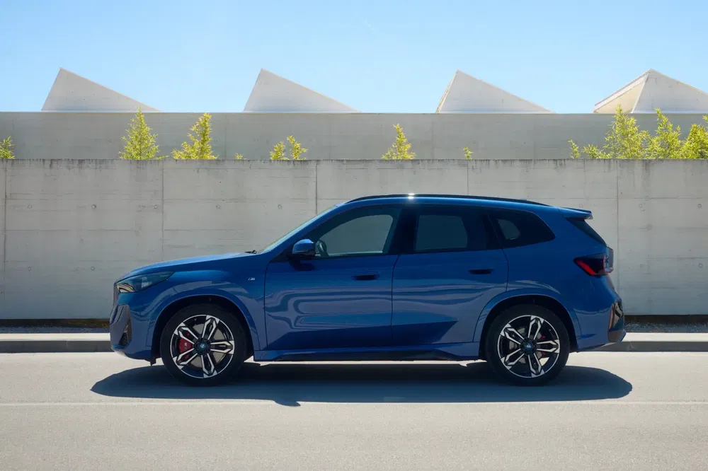 Blauwe BMW X1 geparkeerd bij een moderne muur, elegante en dynamische uitstraling.