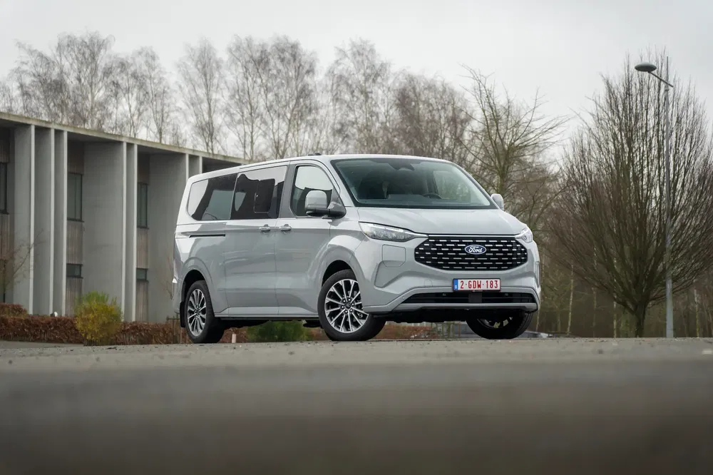 Ford Transit Custom gris garé devant un bâtiment moderne et des arbres dénudés.
